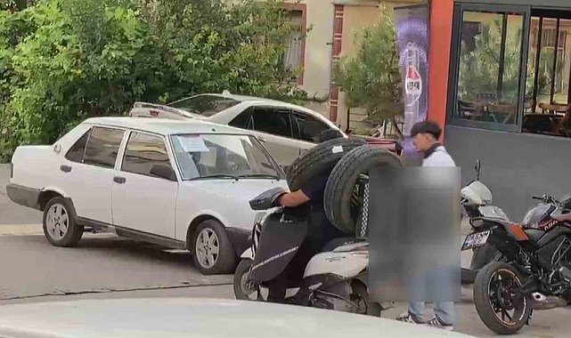 Otomobil lastiğini boynuna asan kuryenin ilginç taşıma yöntemi kameraya yansıdı