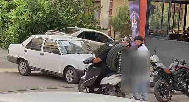 Otomobil lastiğini boynuna asan kuryenin ilginç taşıma yöntemi kameraya yansıdı